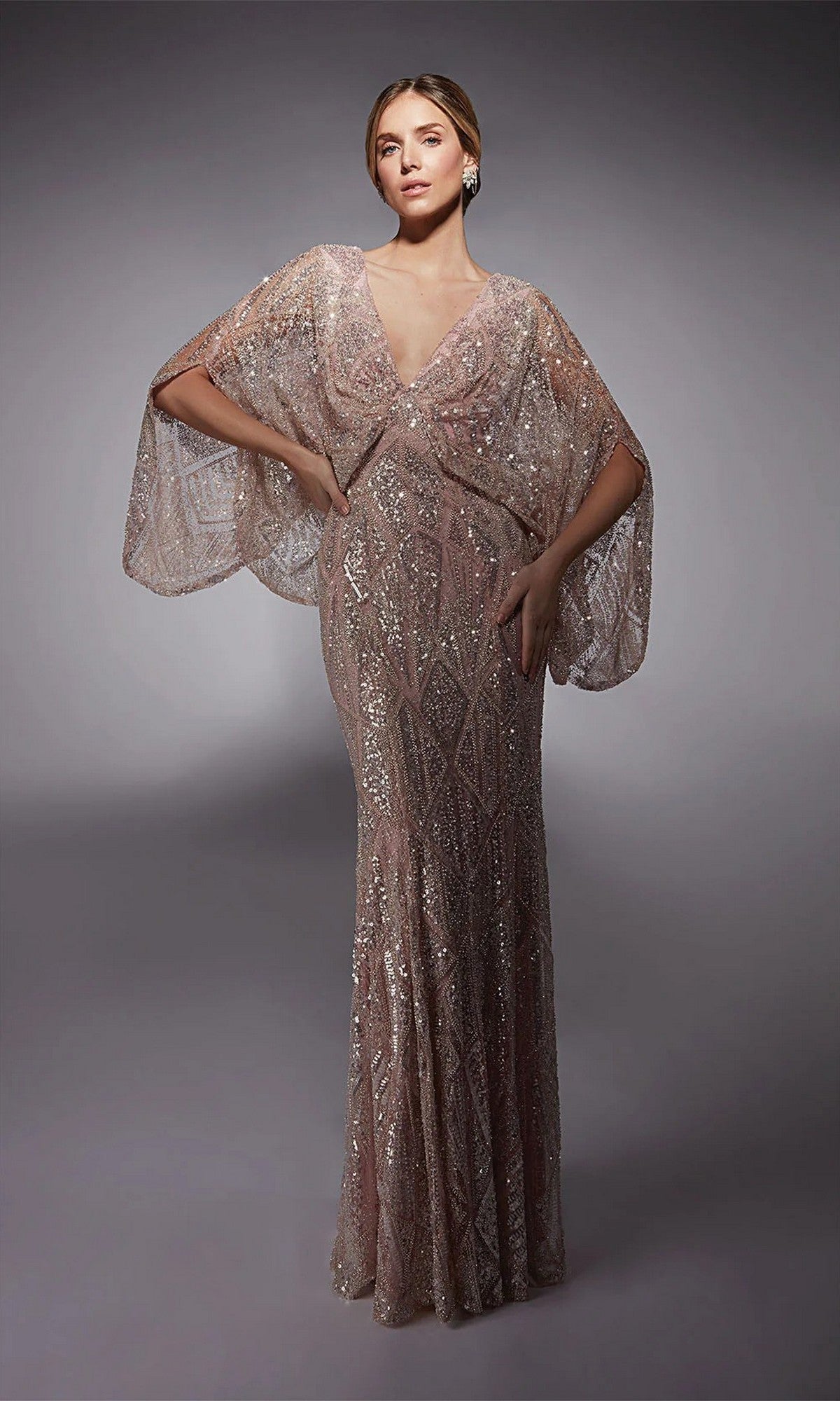 A woman poses in the Long Formal Dress: Alyce 27756, a fitted floor-length evening gown featuring shimmery geometric patterns and sheer cape sleeves—an elegant mother-of-the-bride option.
